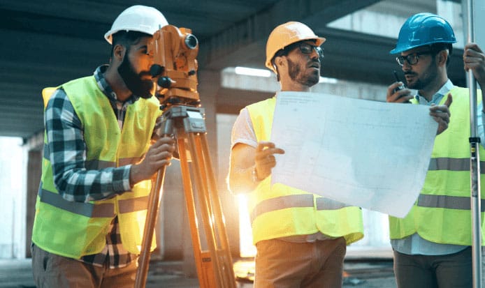 1 person surveying a job site and 1 person looking over blueprints